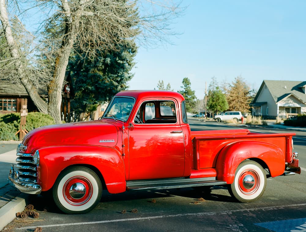 Red 1950s Chevrolet pickup truck with whitewall tires parked on a tree-lined street