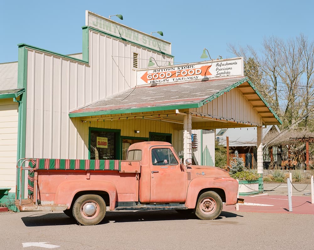 Faded red vintage pickup truck parked in front of an old general store with a Good Food sign