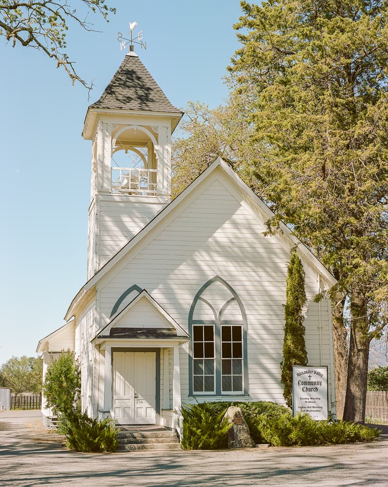White country church with a bell tower framed by evergreen trees under a clear blue sky