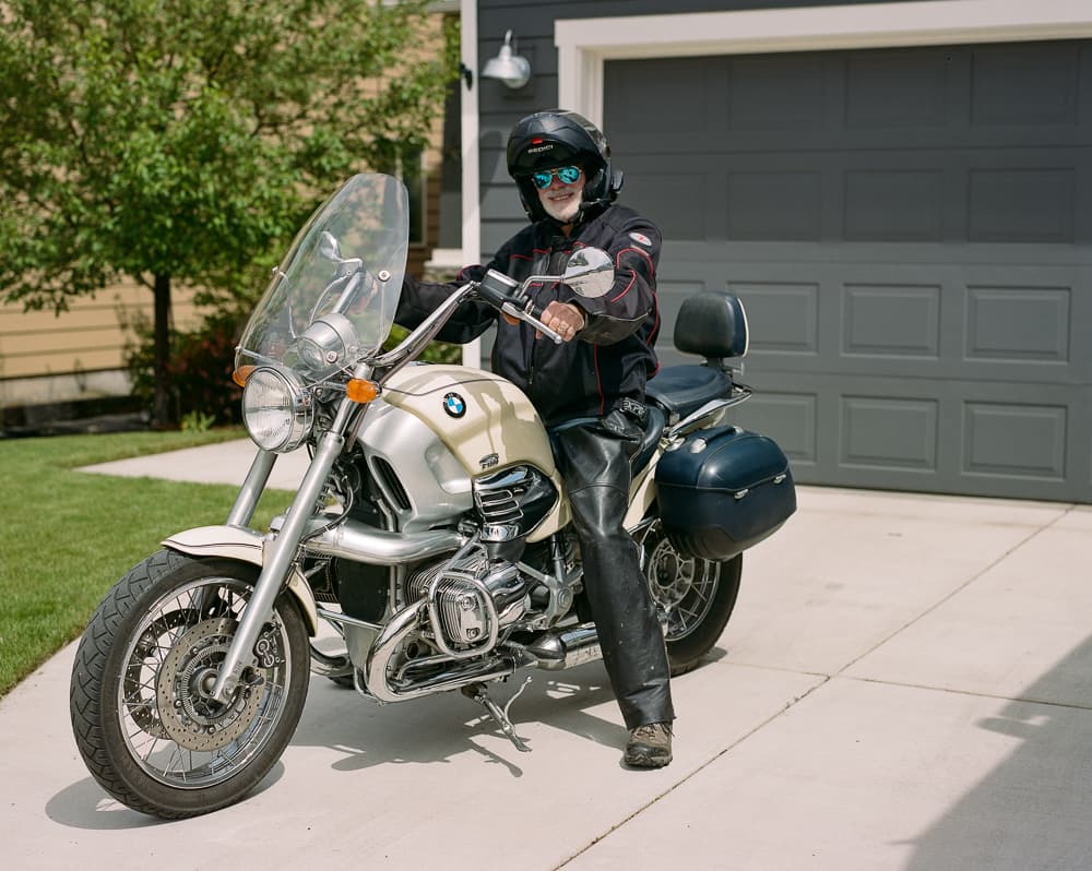 Motorcyclist in helmet and leather jacket seated on a cream BMW touring motorcycle in a driveway