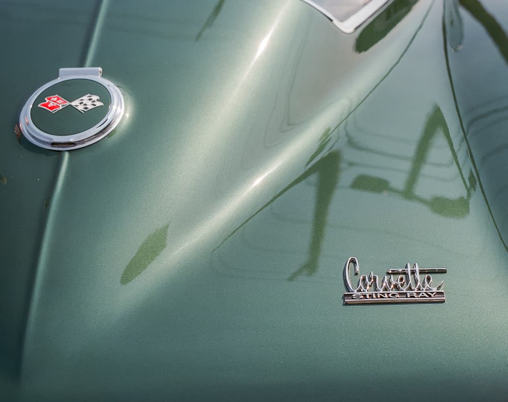 Close-up of a green Corvette Sting Ray hood with crossed-flags badge and chrome emblem