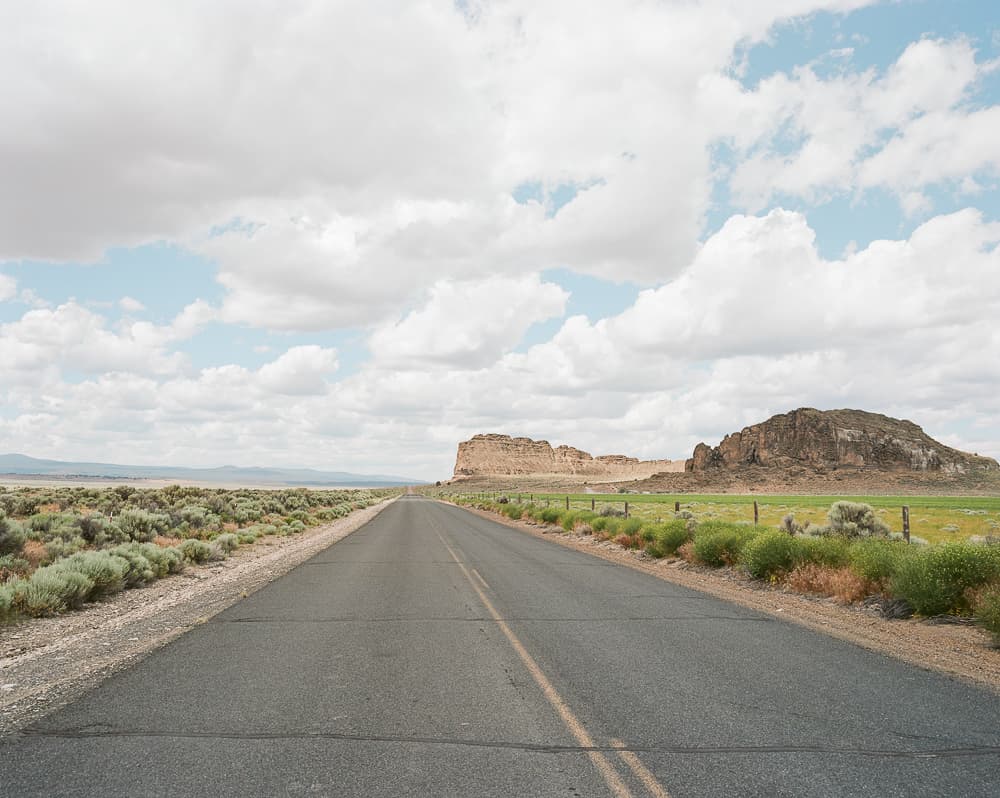 Empty two-lane road running through sagebrush toward desert rock formations