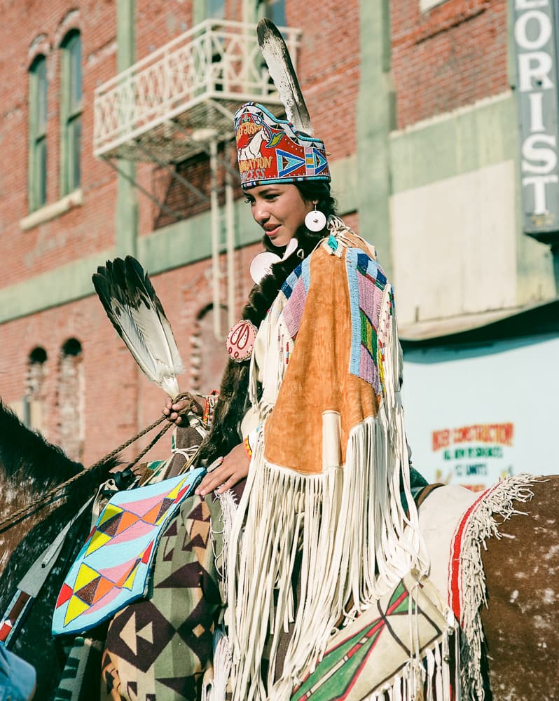 Rider in traditional beaded regalia and feathered headdress on horseback during a street parade