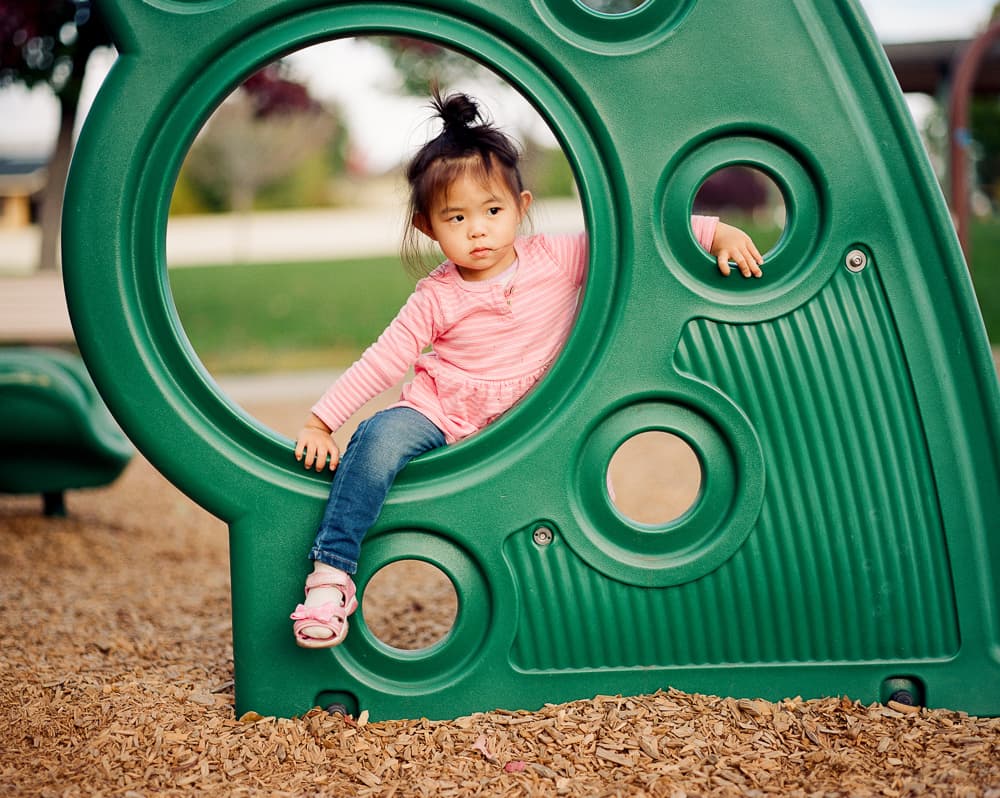 Young girl in pink sitting in the circular opening of a green playground climber