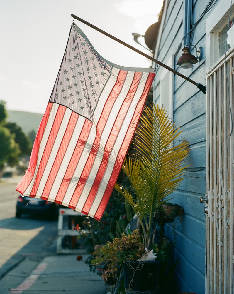American flag hanging from a blue house, backlit by low evening sun