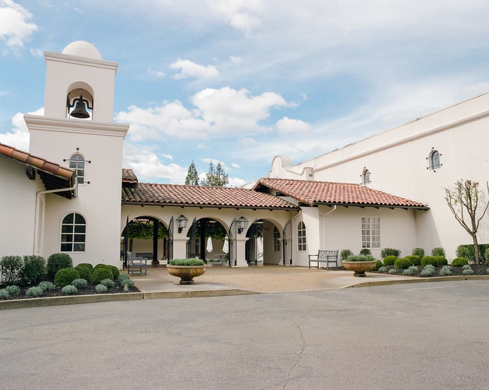 Spanish mission-style building with a bell tower and red tile roofs under a partly cloudy sky